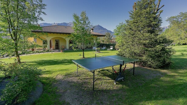 Une maison avec un court de tennis, un espace salon extérieur et une montagne en toile de fond.