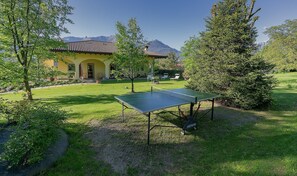 Ein Haus mit Tennisplatz, Sitzgelegenheiten im Freien und einem Berg im Hintergrund.