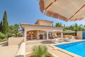 A poolside area with lounge chairs, umbrellas, and a clear blue pool.