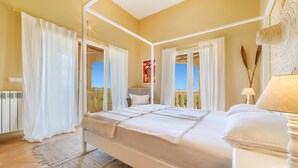 Un dormitorio con cama, cortinas, una ventana con vistas, una lámpara de noche y un adorno en la pared.