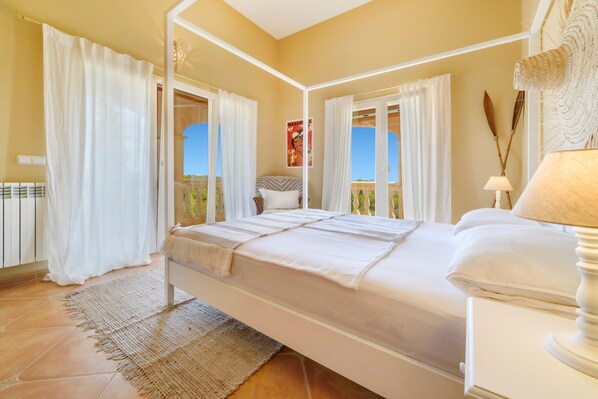 A bedroom with a bed, curtains, a window with a view, a bedside lamp, and a decorative wall piece.