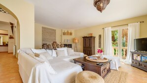 Un salón espacioso con un sofá grande, una chimenea, un televisor y vistas al exterior.