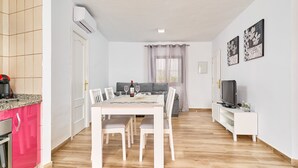 A dining area with a table and chairs, a sofa, a TV on a stand, and a kitchen area with a stove. - Cottage "Casa Loli" with Mountain View, Private Pool & Terrace (Frigiliana)