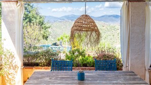 Un espace extérieur abrité, aménagé avec une table et des chaises, un luminaire suspendu, et offrant une vue sur un paysage montagneux.