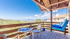 A wooden deck with a swing chair, a small table, and a view of distant mountains.