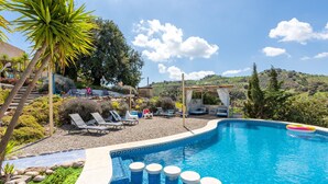 A swimming pool with lounge chairs, a pergola, and a view of hills.