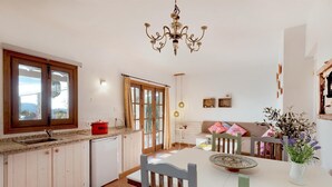 Une cuisine avec une fenêtre, un faitout rouge, un lustre, une table à manger avec des chaises et un canapé.