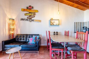 A cozy living area with a black leather sofa, a wooden dining table with red chairs, and a wall with various signs.