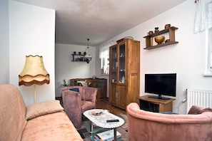 A living room with a sofa, armchair, coffee table, TV, wooden cabinet, and a lamp.
