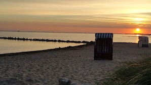 A beach with a chair and a cooler, a calm sea, and a sunset in the background. - Ostseepanorama Heiligenhafen – Apartment with Sea View (Heiligenhafen)