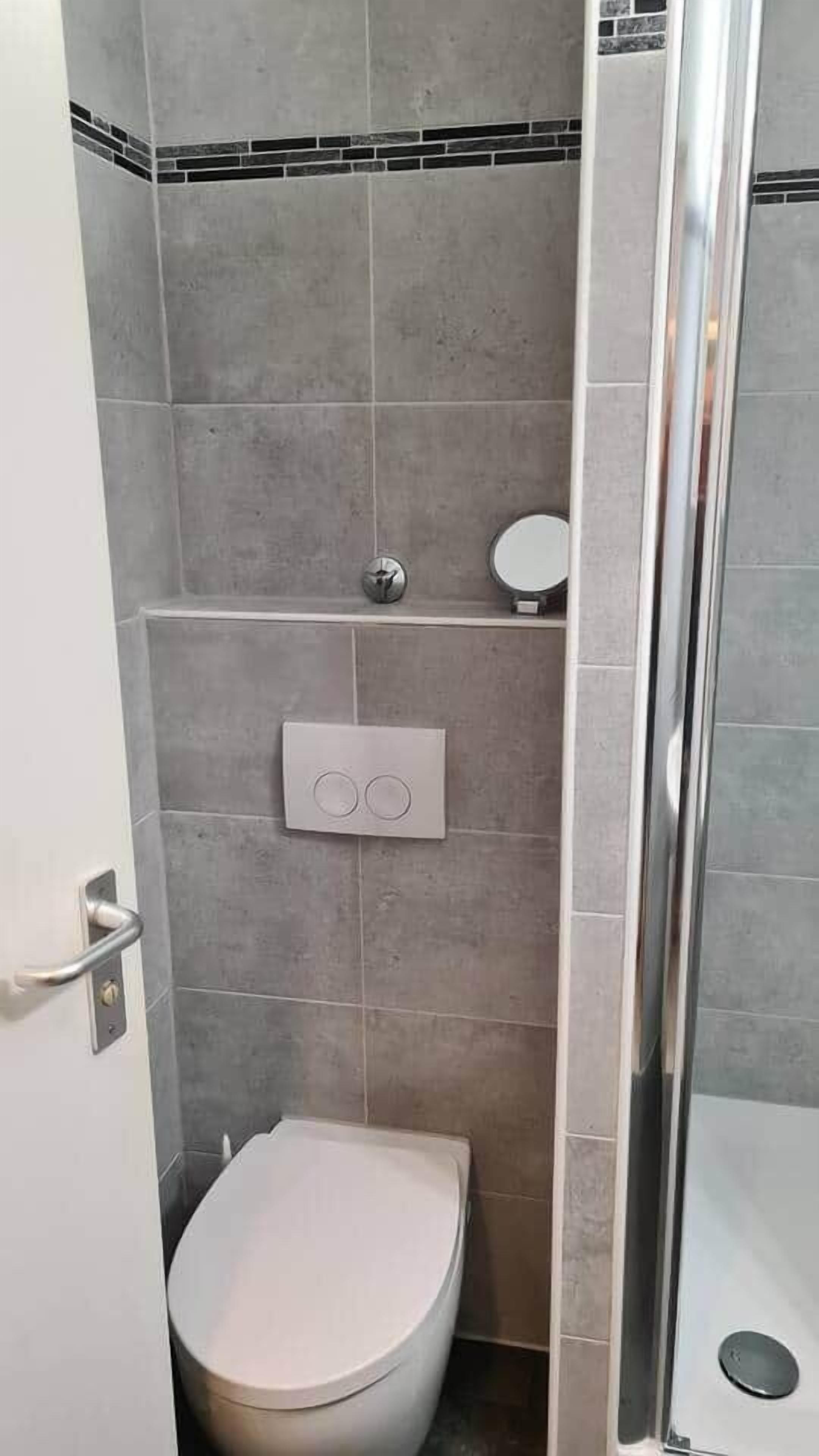 A bathroom with a toilet, a shower, and a wall-mounted control panel.
