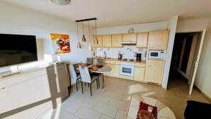 A modern kitchen with a dining area, a TV, and a clock on the wall. - Ostseepanorama Heiligenhafen – Apartment with Sea View (Heiligenhafen)