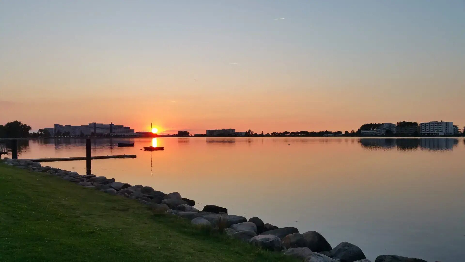 A calm lake at sunset with buildings in the background.