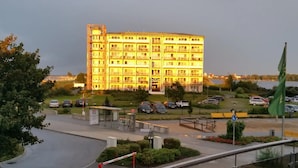 A multi-story hotel with a central courtyard, a flag, and a parking area. - Ostseepanorama Heiligenhafen – Apartment with Sea View (Heiligenhafen)