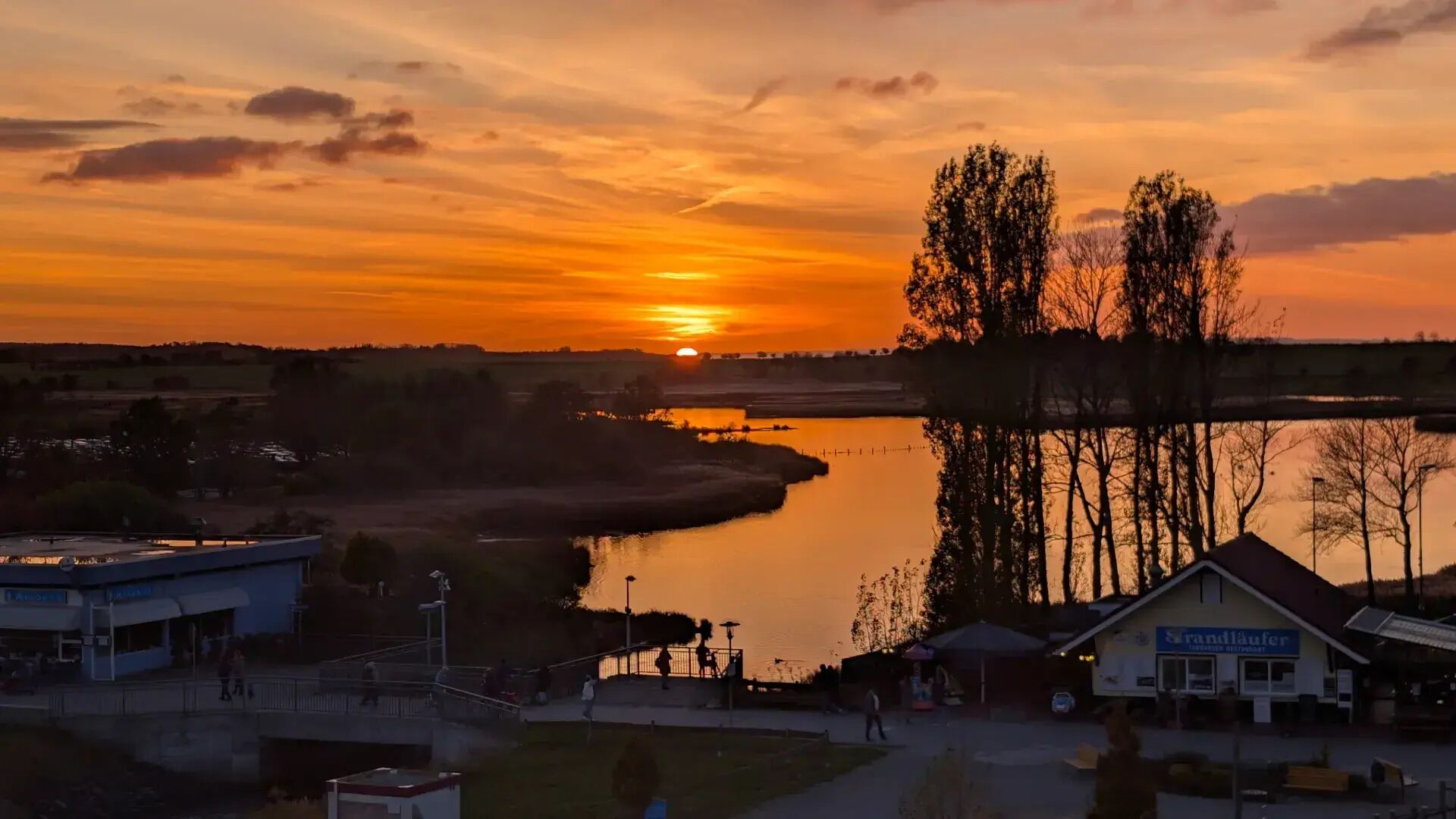 A riverside view with a sunset, a bridge, and a building with a sign.