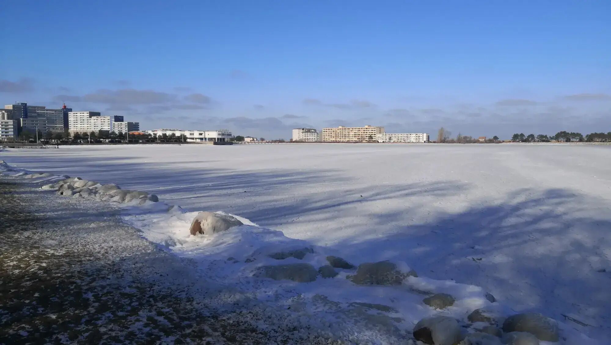 A frozen lake with buildings in the background.