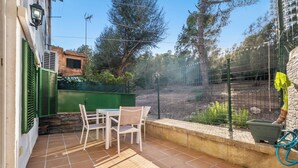 Eine Terrasse mit Tisch und Stühlen, ein grüner Zaun und eine Steinmauer.
