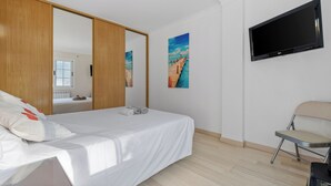 Ein Schlafzimmer mit einem Bett, einem Fernseher, einem Sessel und einem Bild an der Wand.