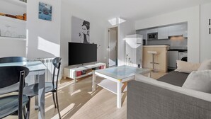 Ein modernes Wohnzimmer mit Flachbildfernseher, einem Essbereich mit Stühlen, einer Couch und einer Küchenzeile mit Geräten.