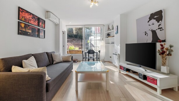 Ein modernes Wohnzimmer mit einer Couch, einem Glastisch, einem Fernseher auf einem weißen Schrank und Kunstwerken an den Wänden.