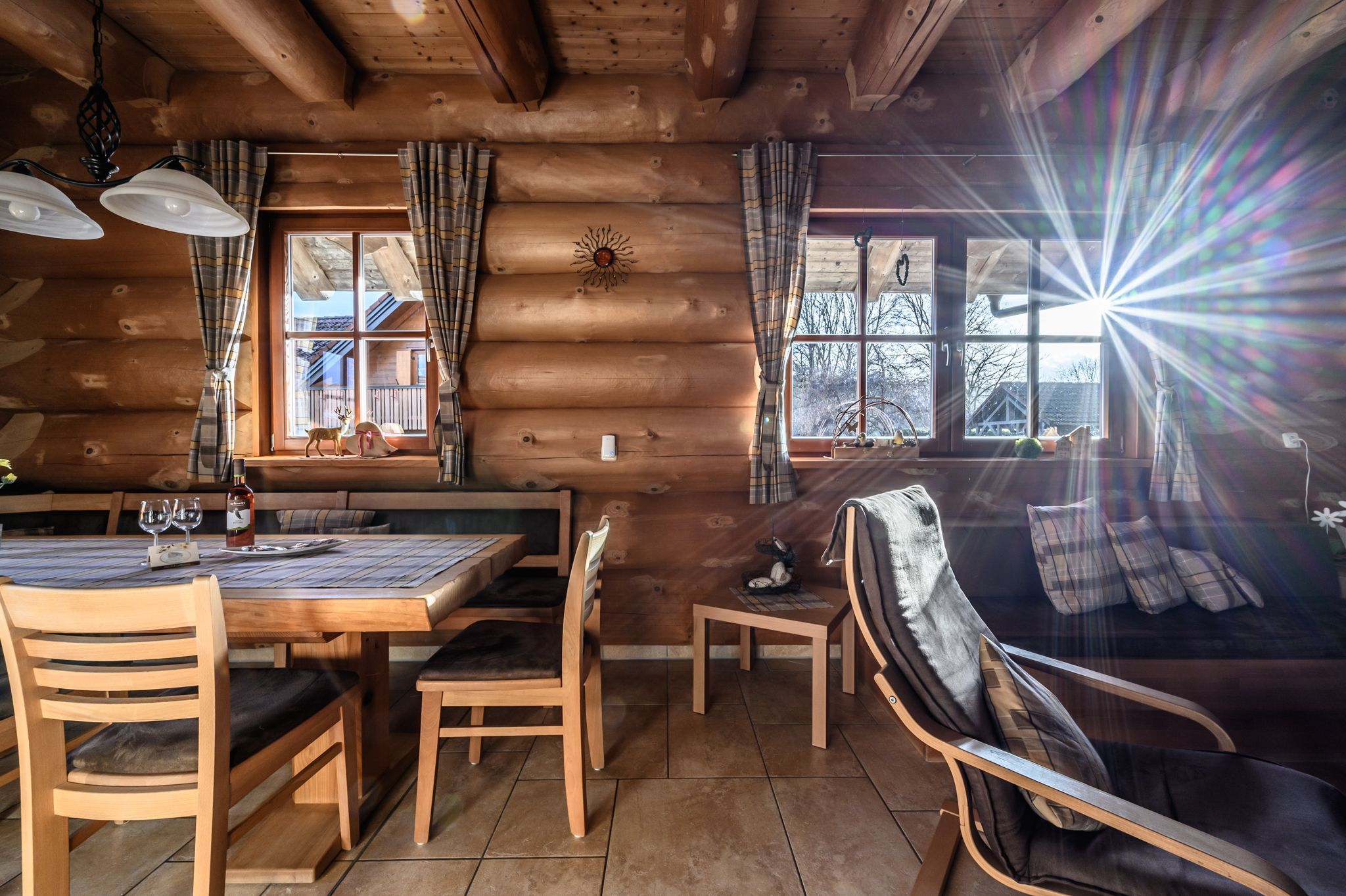 L’intérieur d’un chalet en bois, avec une table à manger, des chaises, un canapé et une fenêtre avec des rideaux.