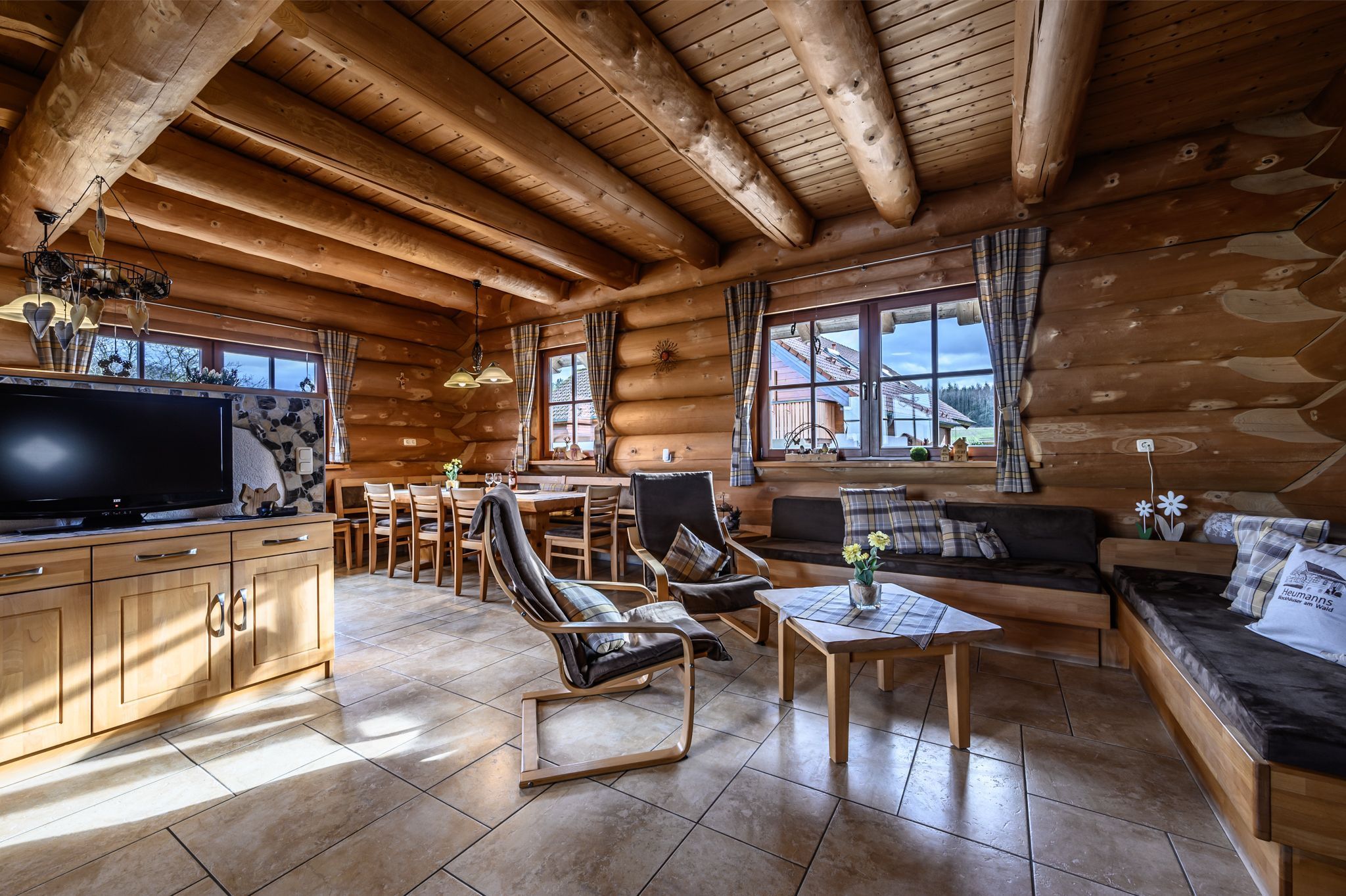 A log cabin interior with a TV, seating area, dining space, and large windows.