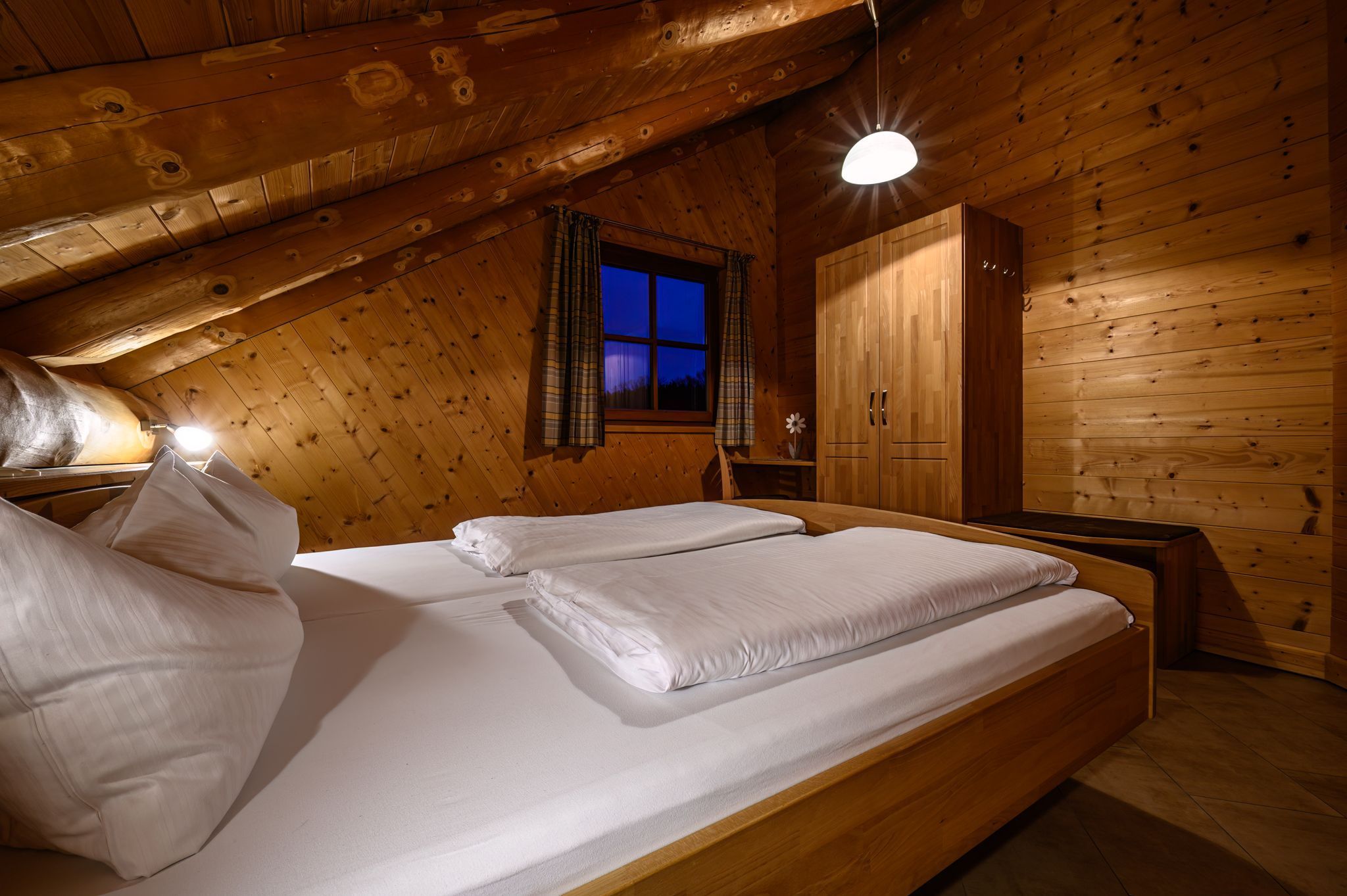 Une chambre dans une cabane en bois, avec un lit, une armoire et une fenêtre avec des rideaux.