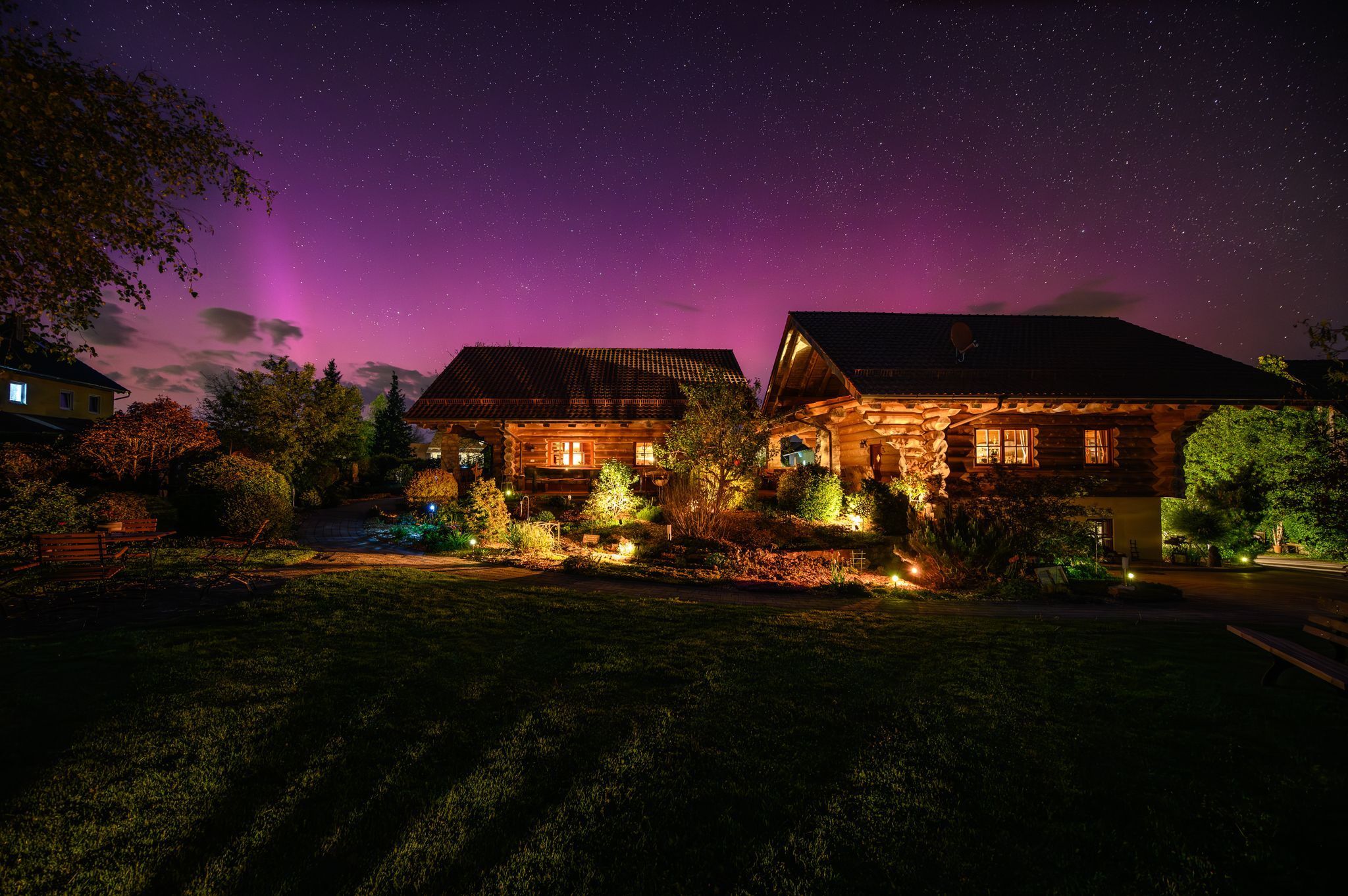 A log cabin with a starry night sky, illuminated windows, and a well-maintained garden.