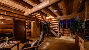 A log cabin interior with a wooden staircase, a dining area with a table and chairs, and a kitchen area. - Natural log house Morgensonne - Heumann's log houses by the forest (Pottenstein)