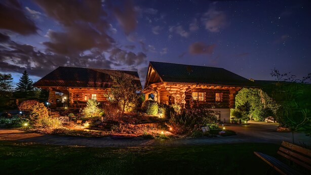 A log cabin with a porch and a well-lit garden at night. - Natural log house Morgensonne - Heumann's log houses by the forest (Pottenstein)