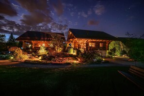 A log cabin with a porch and a well-lit garden at night. - Natural log house Morgensonne - Heumann's log houses by the forest (Pottenstein)