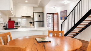 A modern kitchen with white cabinets, stainless steel appliances, and a dining area with a wooden table and chairs. - THe Iceworks - COnverted ice factory in the centre of Fremantle (Fremantle)