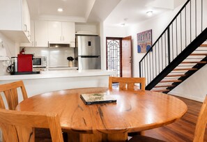 Une cuisine moderne avec des meubles blancs, des appareils en acier inoxydable et un coin repas comprenant une table et des chaises en bois.