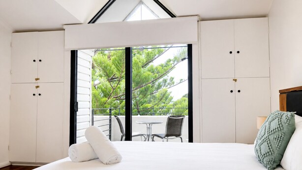 A bedroom with a large bed, a balcony with a table and chairs, and a view of trees. - THe Iceworks - COnverted ice factory in the centre of Fremantle (Fremantle)