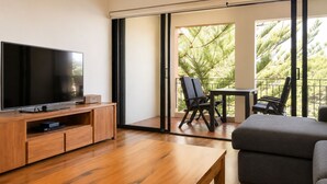 A modern living room with a flat-screen TV, wooden furniture, a balcony with chairs, and a view of greenery. - THe Iceworks - COnverted ice factory in the centre of Fremantle (Fremantle)