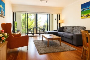 A modern living room with a sofa, armchair, coffee table, and a view of the outdoors through large windows.