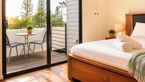 A bedroom with a wooden bed, a small balcony with chairs, and a view of trees. - THe Iceworks - COnverted ice factory in the centre of Fremantle (Fremantle)