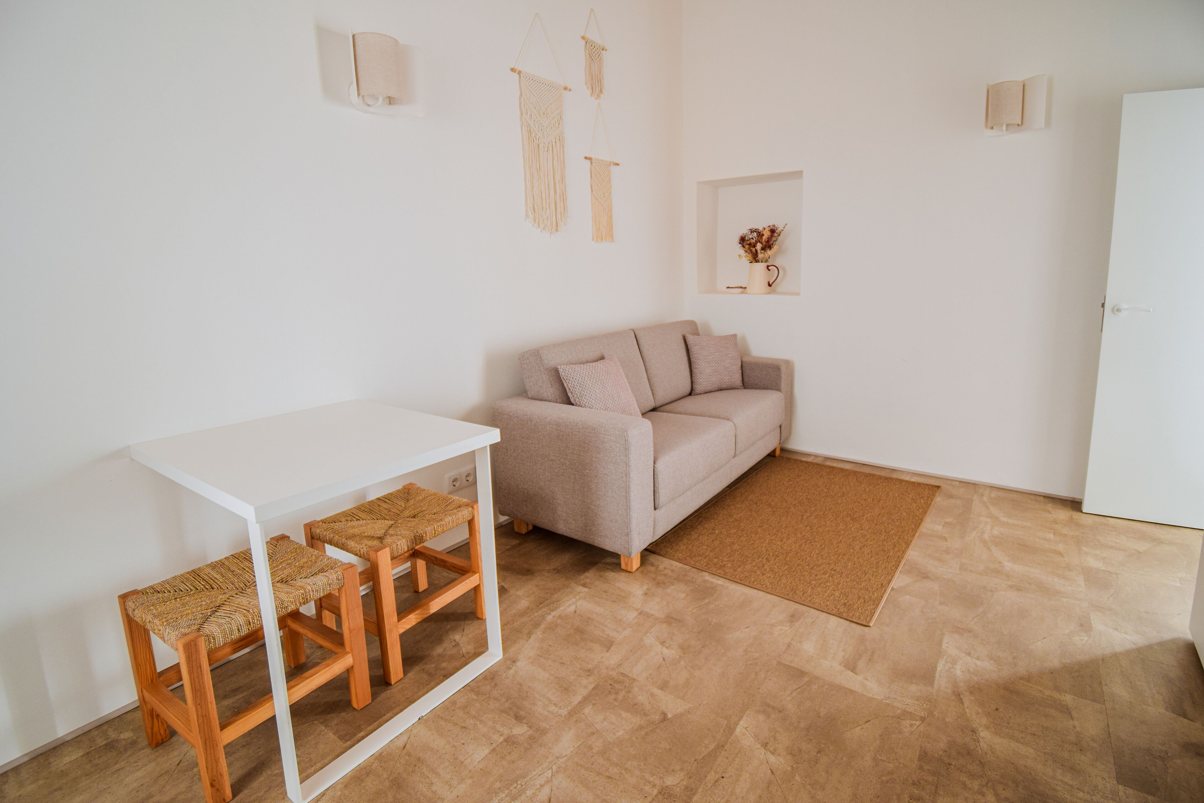 A minimalist living room with a white sofa, a small table, and two wicker chairs.