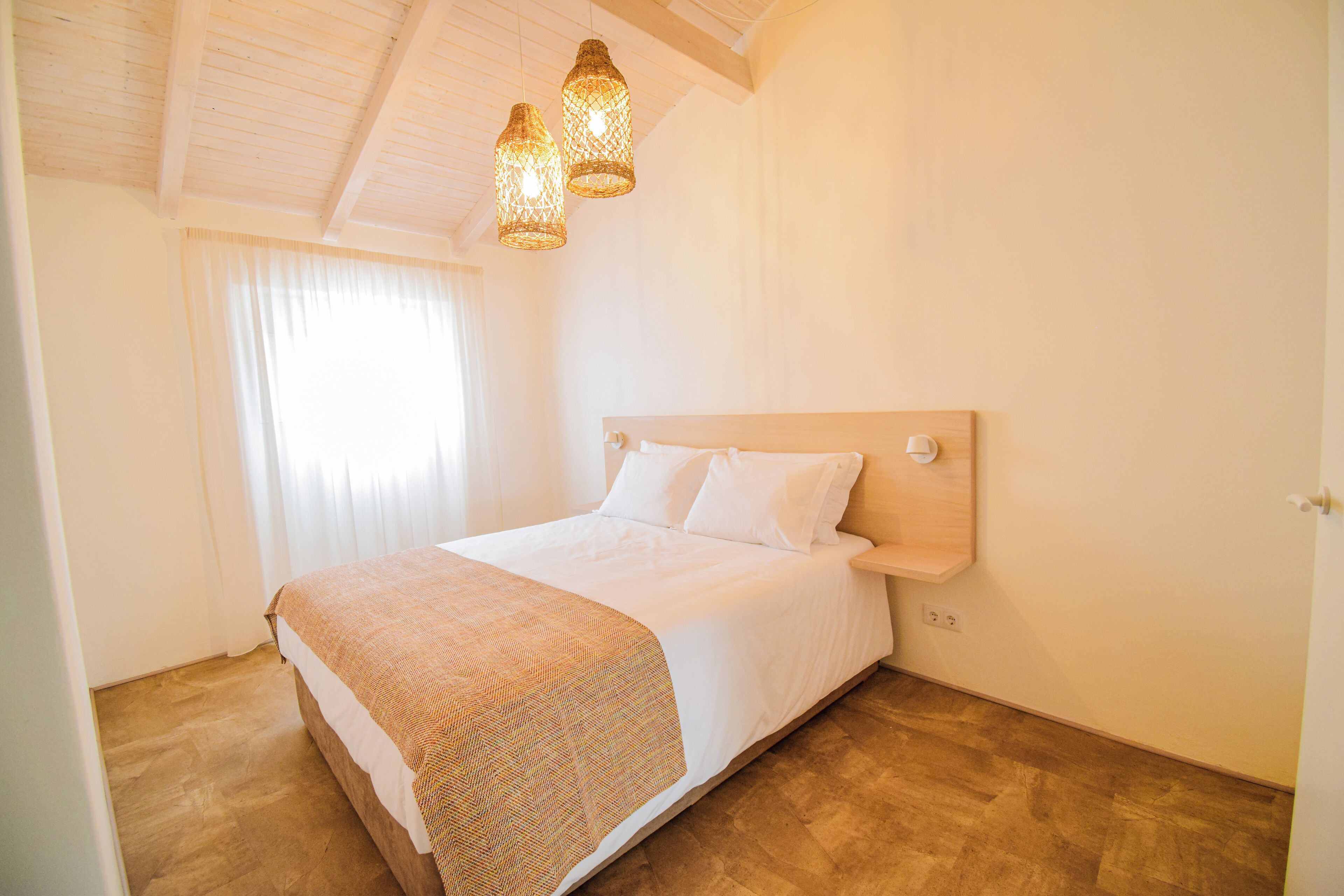 Un dormitorio con cabecera de madera, una cama grande con ropa blanca y dos lámparas colgantes.