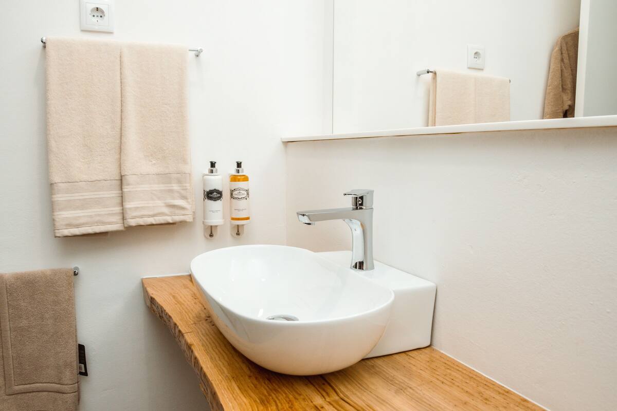 A bathroom with a white sink, wooden countertop, and two beige towels hanging on hooks.