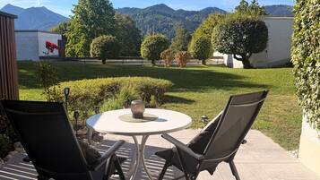 Une terrasse extérieure avec une table ronde et deux chaises, entourée de verdure et offrant une vue sur les montagnes.