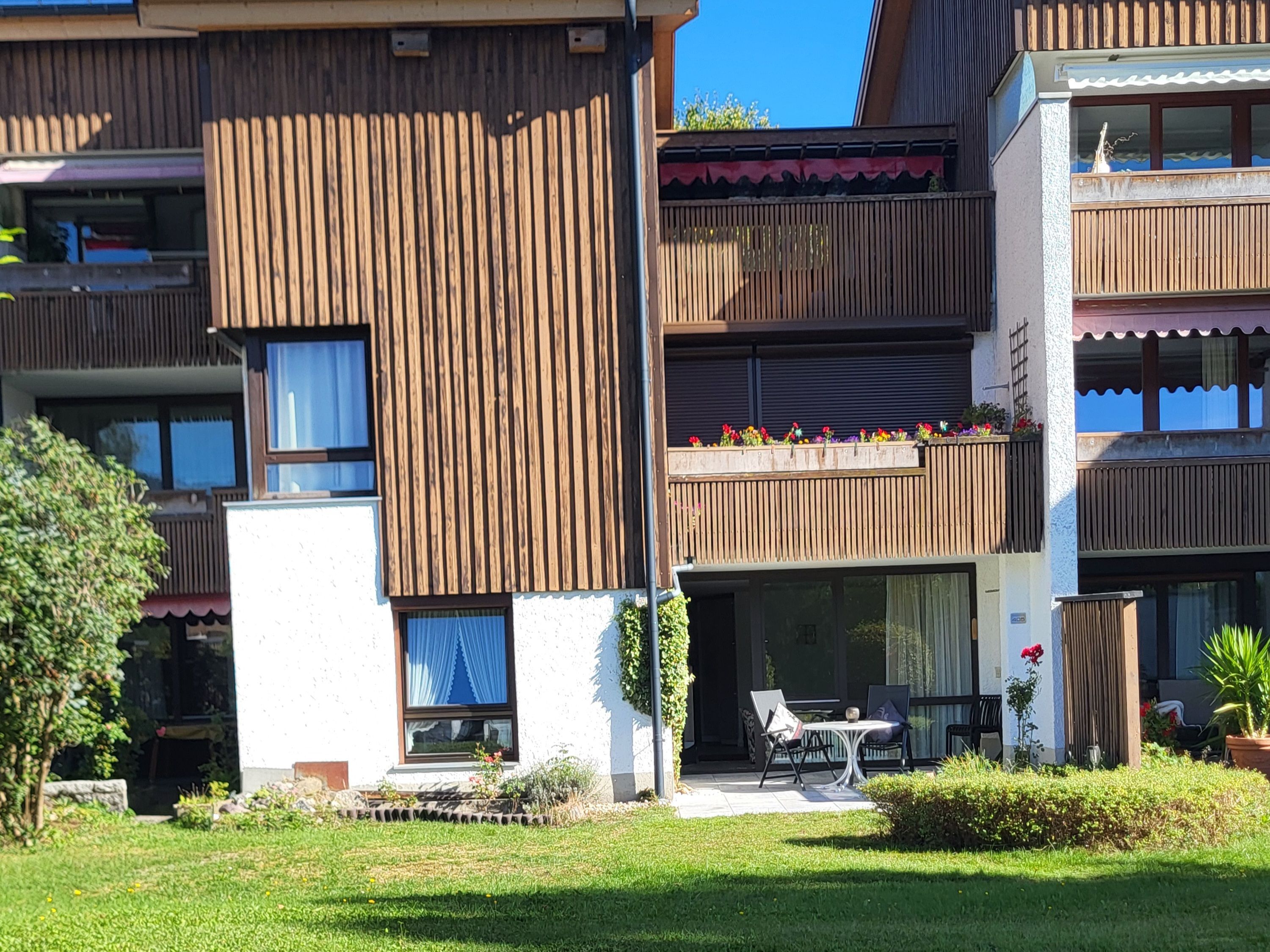 Un immeuble résidentiel à plusieurs étages, doté de balcons, d’un petit espace extérieur aménagé en coin salon et d’un jardin.