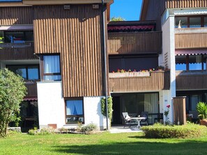 Un immeuble résidentiel à plusieurs étages, dot é de balcons, d’un petit espace extérieur aménagé en coin salon et d’un jardin.