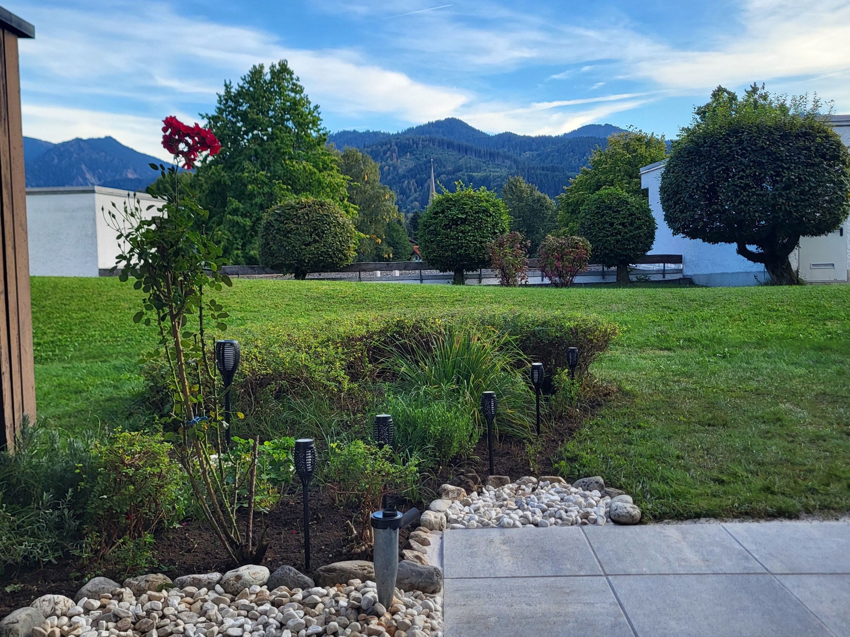 Ein angelegter Garten mit einem Weg, verschiedenen Pflanzen und Blick auf ferne Berge.