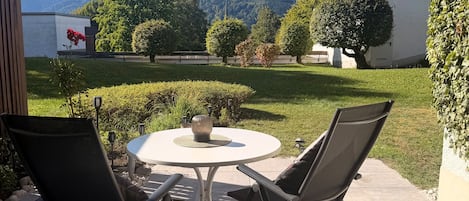 Une terrasse extérieure avec une table ronde et deux chaises, entourée de verdure et offrant une vue sur les montagnes.