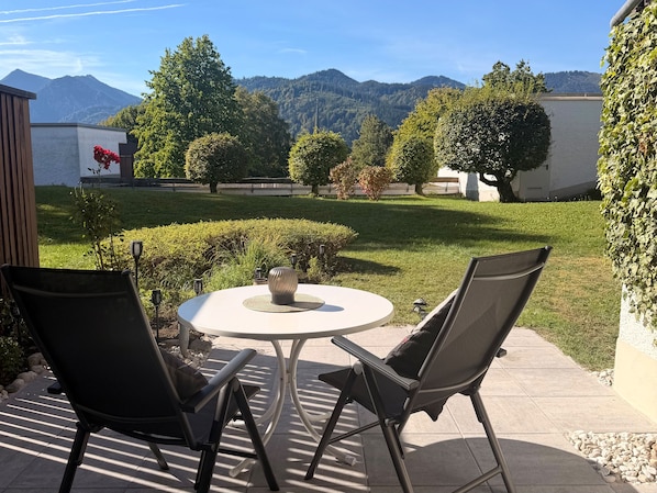 Une terrasse extérieure avec une table ronde et deux chaises, entourée de verdure et offrant une vue sur les montagnes.