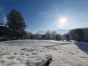 Un paysage enneigé avec des bâtiments et des arbres, un ciel dégagé et des montagnes à l'horizon.