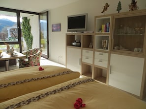 Ein Schlafzimmer mit zwei Betten, einem Fernseher, einer Schrank mit Glastüren und Blick ins Freie.