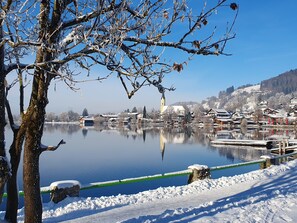 Schneebedeckte Landschaft mit einem Gewässer, Gebäuden und einer Kirche.