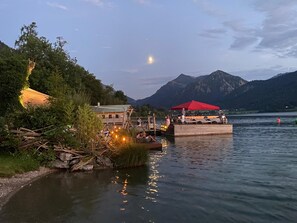 Eine hölzerne Konstruktion am Seeufer mit rotem Baldachin, umgeben von Bäumen und Bergen.
